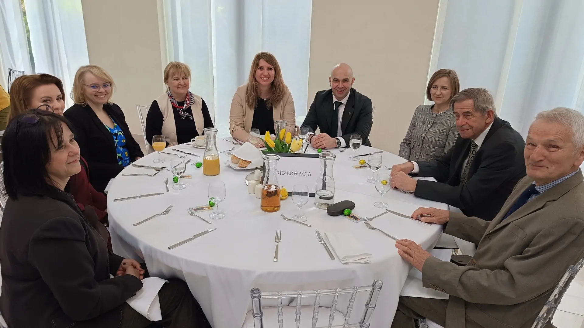 Zdjęcie uśmiechniętych osób siedzących przy stole i pozujących wspólnego do zdjęcia